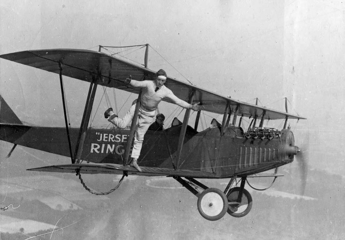 A wing walker stands on one leg on the wing of a Curtiss ‘Flying Jenny’ biplane in the air above New Jersey, 1920.