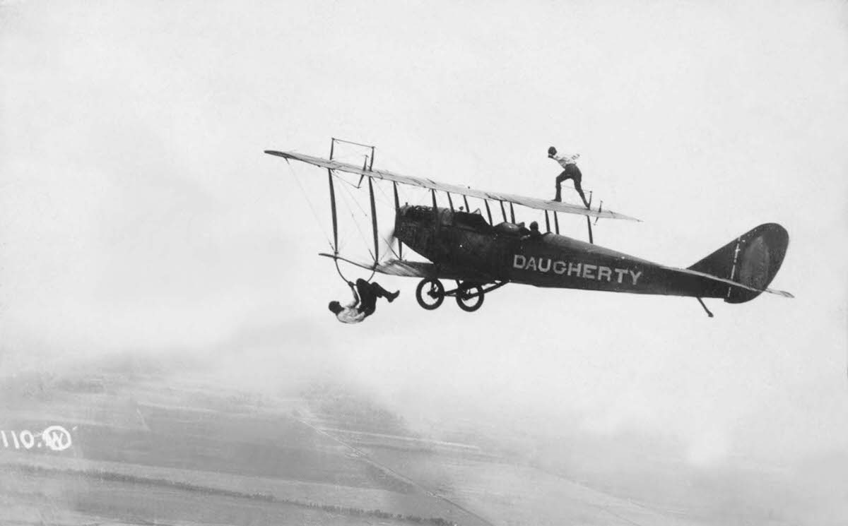 Wing walkers show off above and below a biplane, 1920.