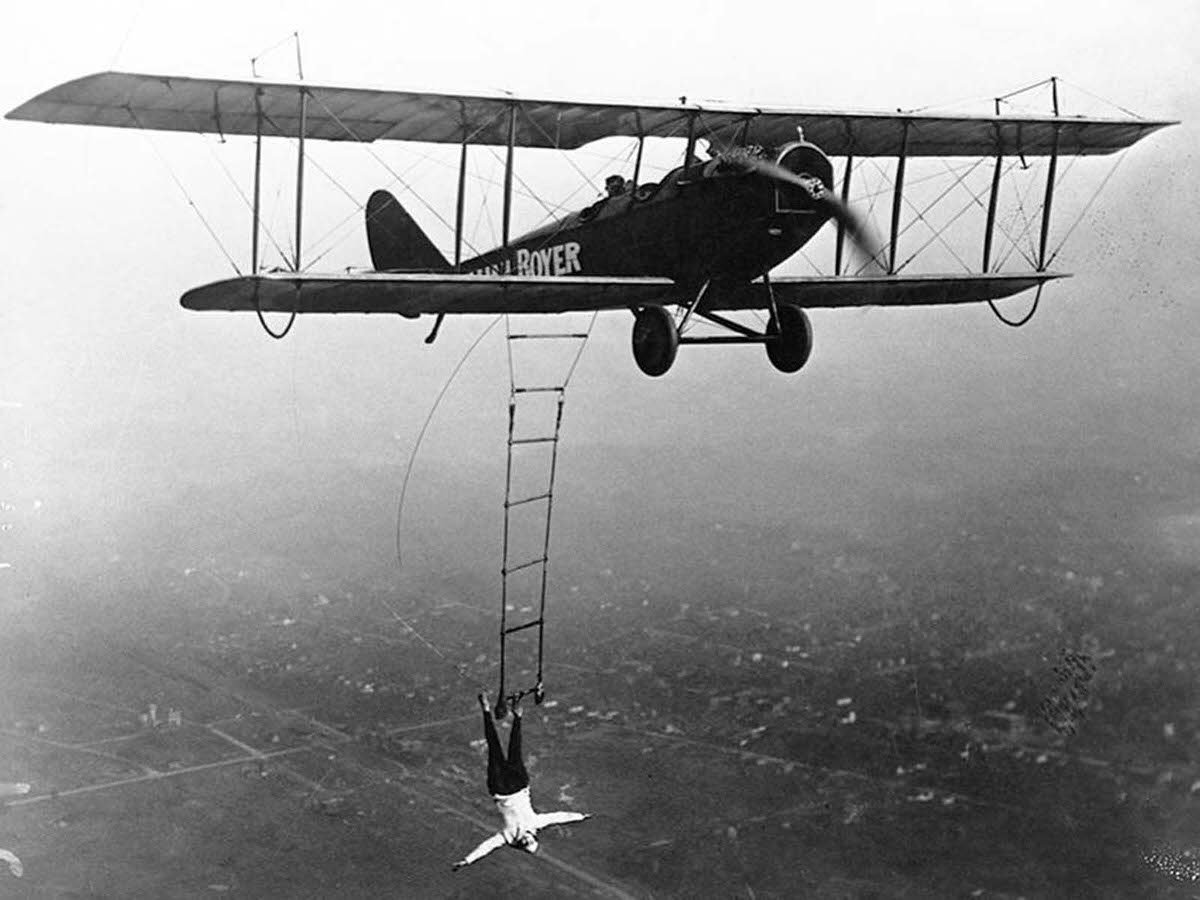 Lillian Boyer hanging from right wing boom using her right hand, 1920s.