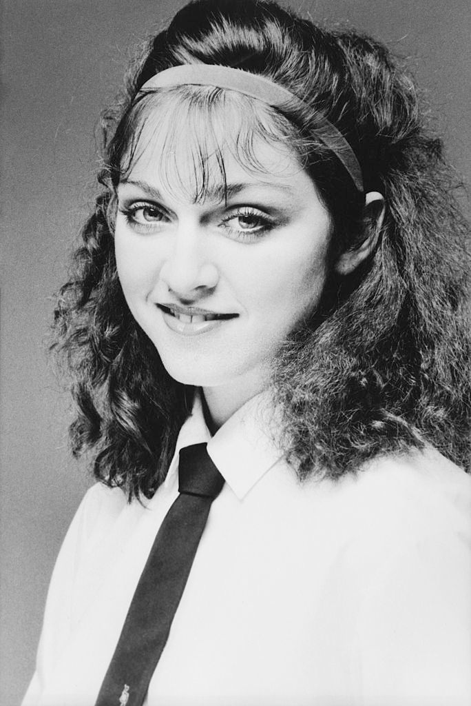 Madonna smiling while wearing a white cotton shirt with a dark tie, 1978.