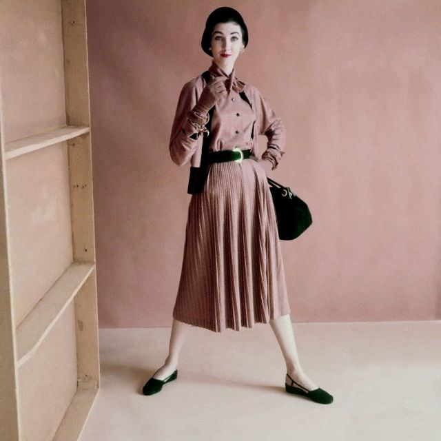 Model is wearing a wool jersey blouse that ties at the neck, a wool jersey cardigan with black knit ribbing, and a slim pleated skirt in matching wool jersey, 1952
