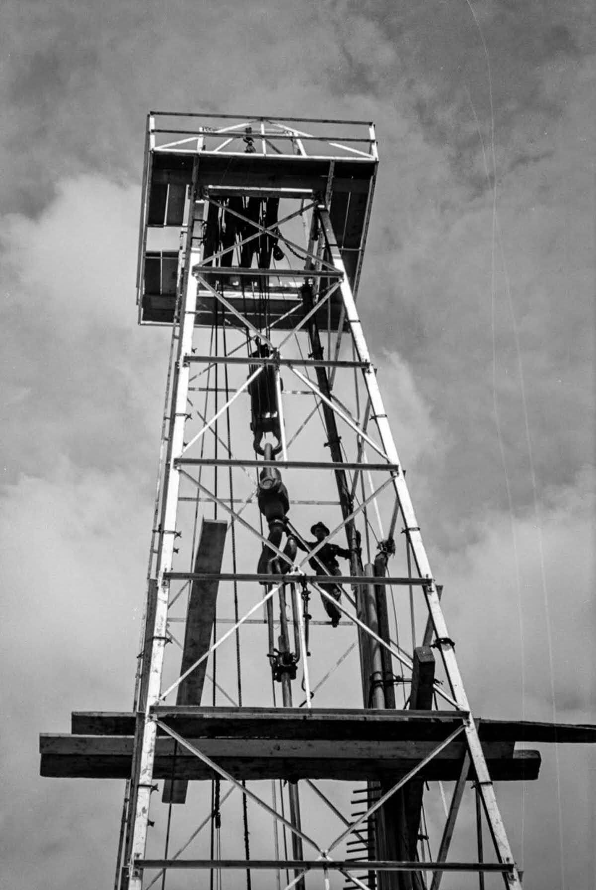 A worker holds onto the traveling block near the top of the derrick.