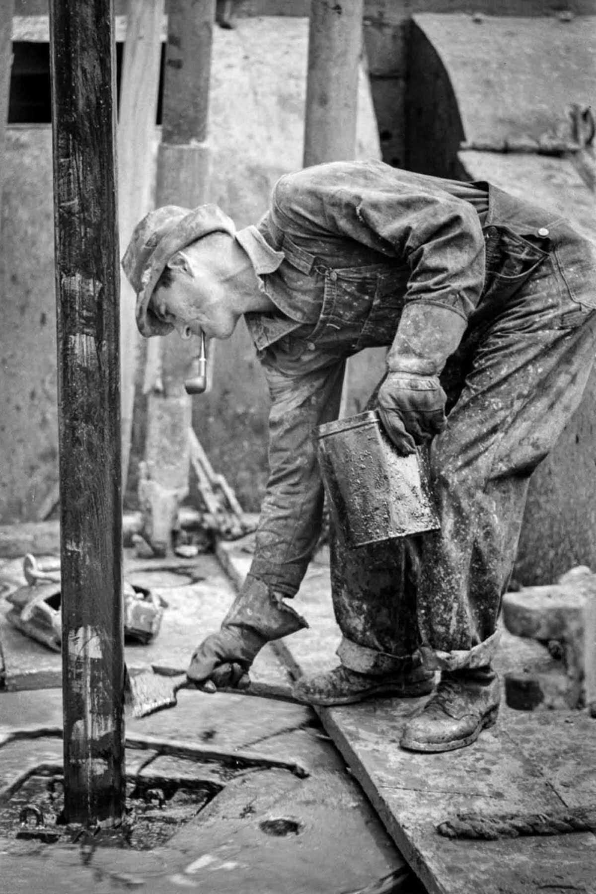 A worker chews on a pipe while applying grease to a drill stem.