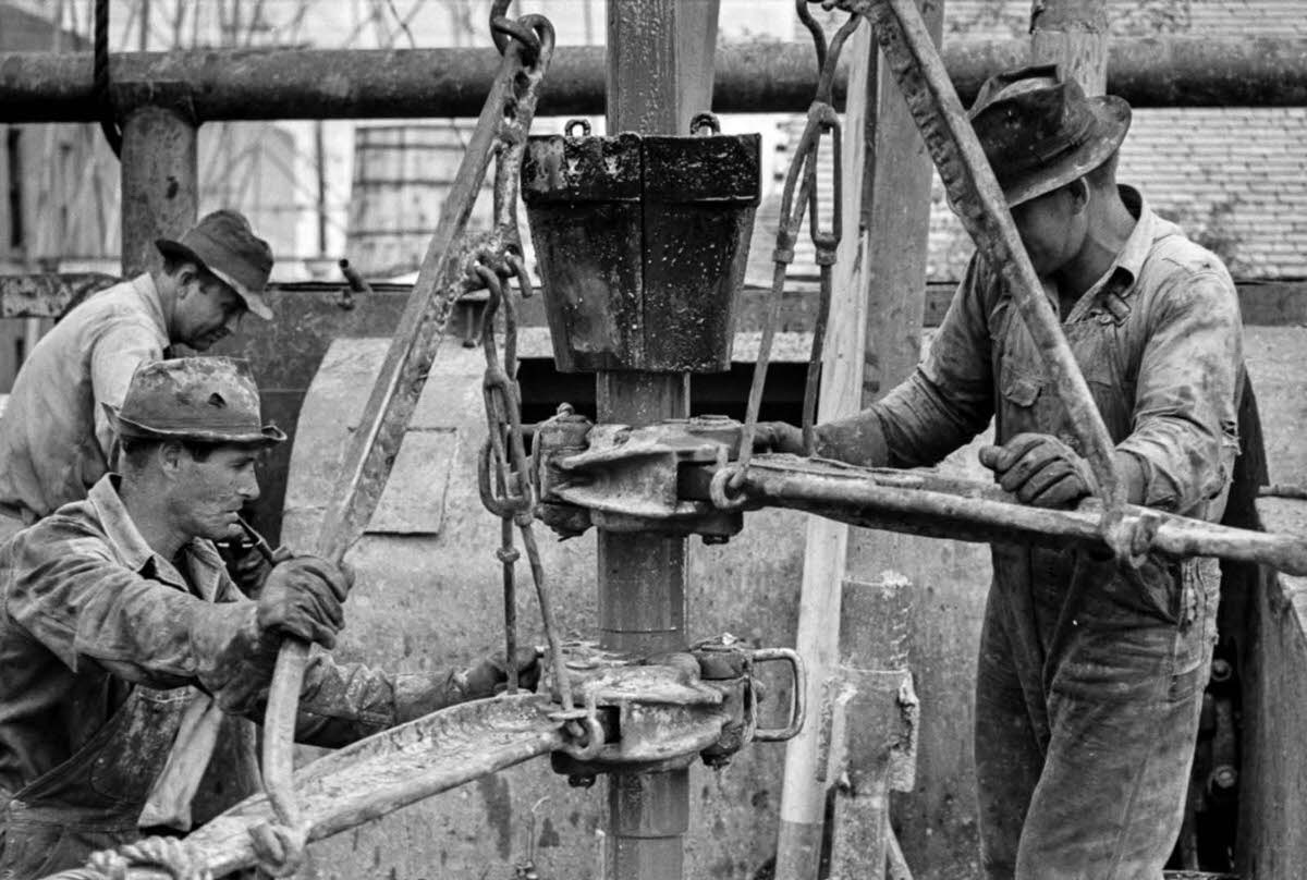 Workers use pipe wrenches to screw together two lengths of pipe.