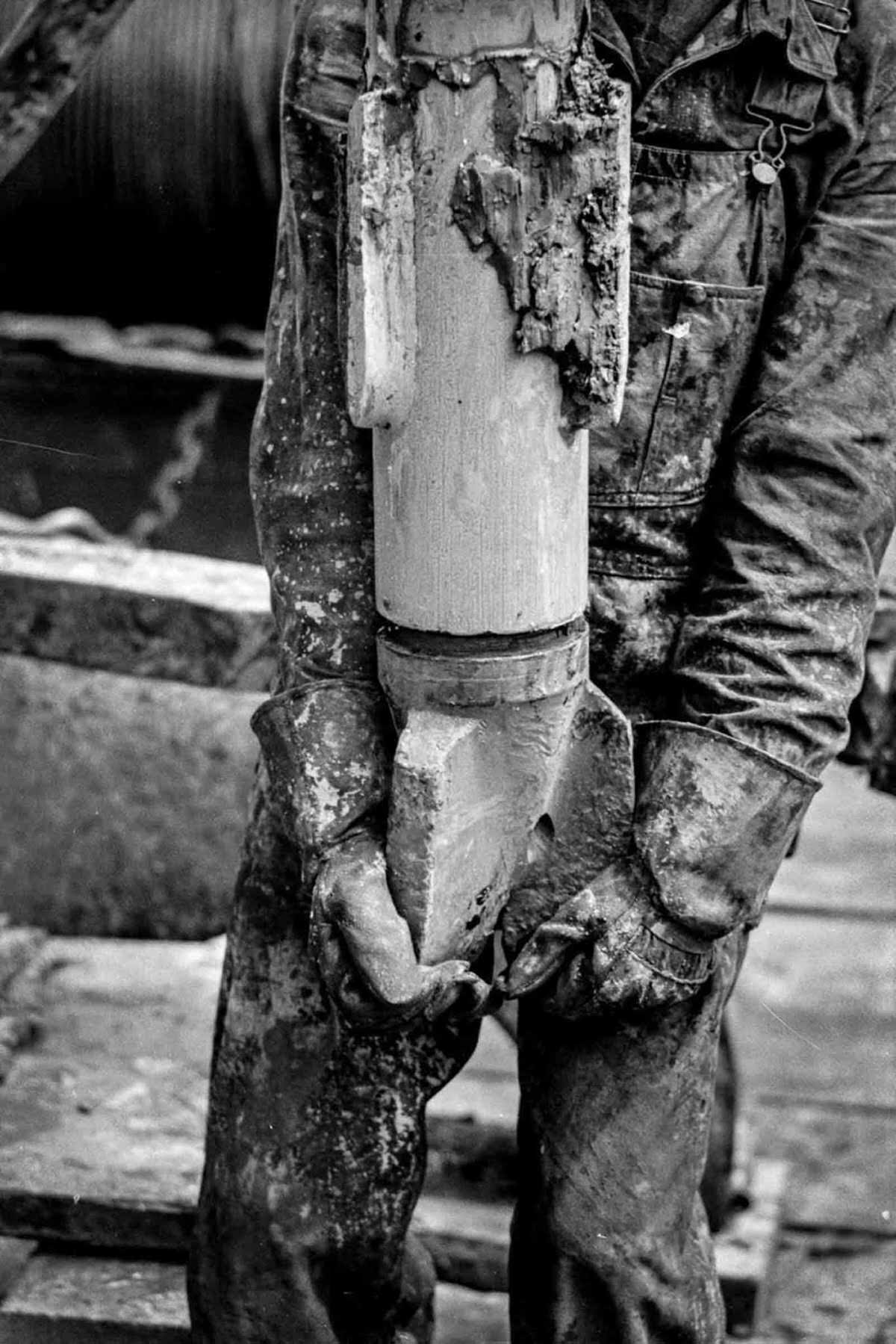 A roughneck holds a mud-caked drill bit.