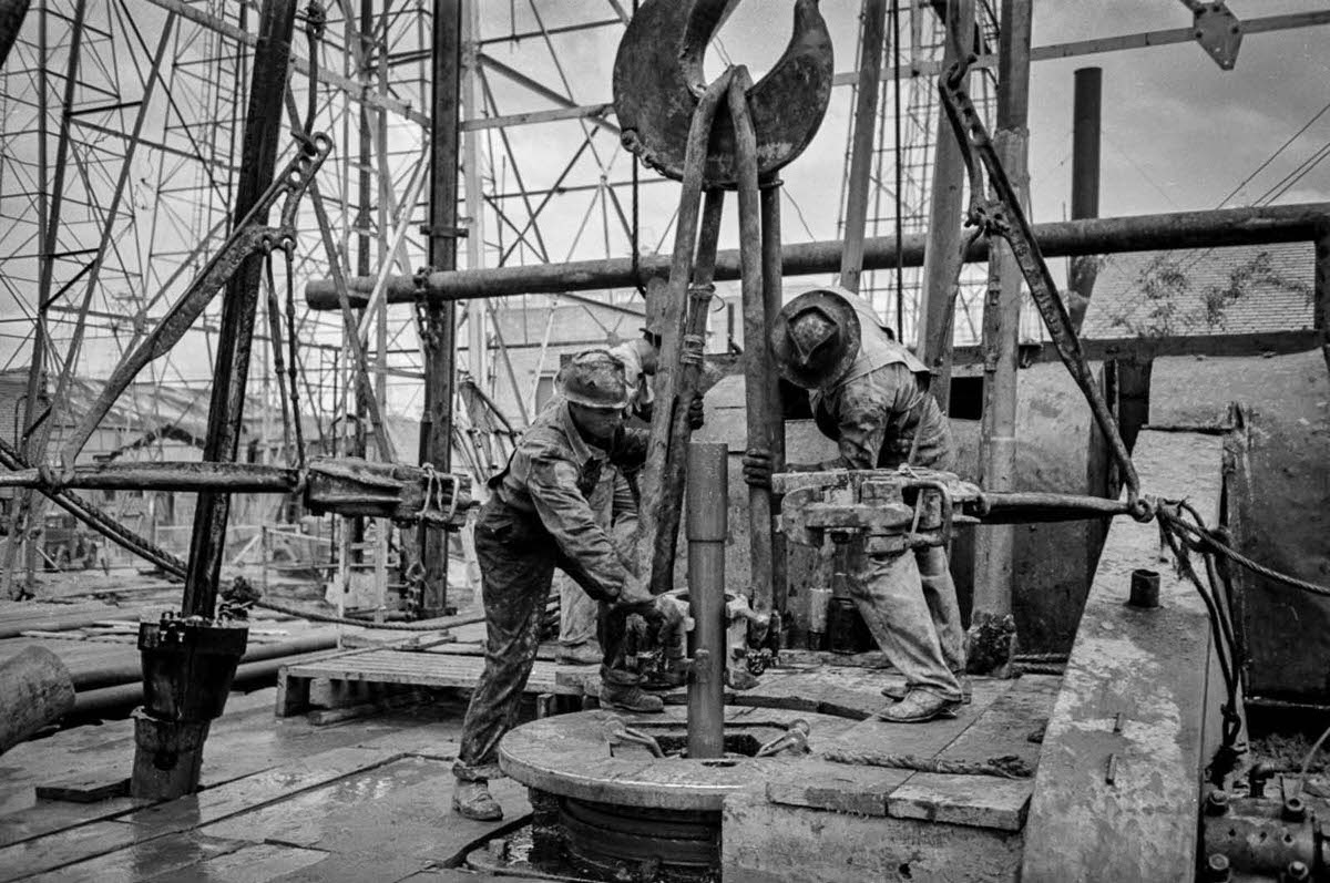 Workers put a clamp in place to bring up a section of drill pipe.