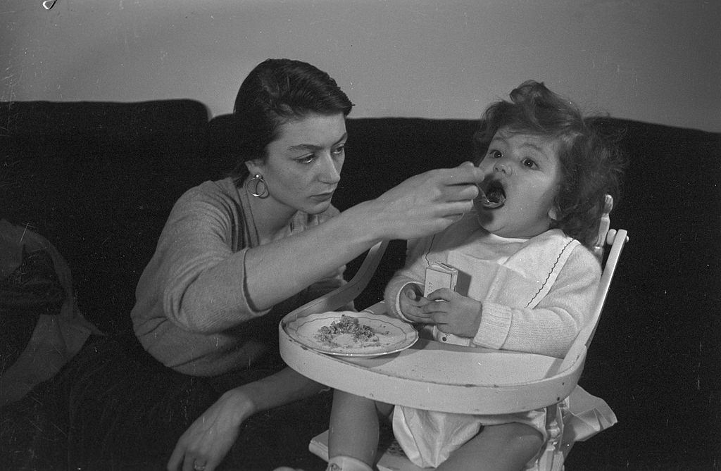 Anouk Aimée feeding her daughter, 1955.