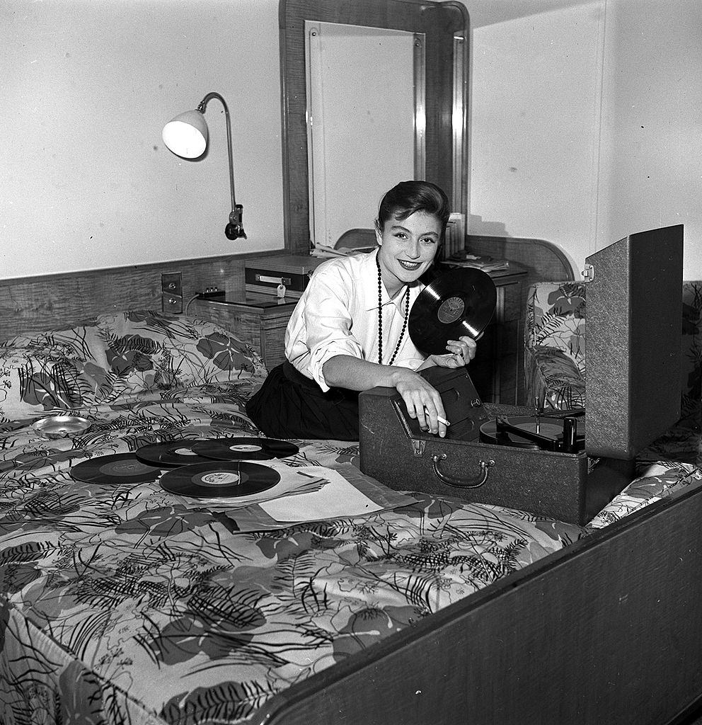 Anouk Aimee is pictured playing music on a record player in her room at the Savoy Hotel, 1954.