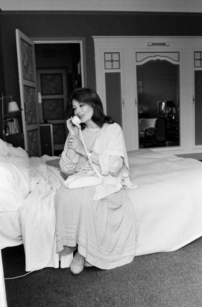 Anouk Aimée telephoning, sitting on the bed in her bedroom, 1980.