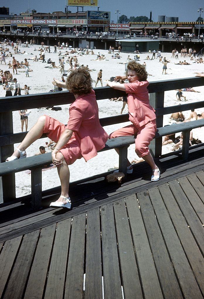 Identical twins dressed alike look out over the Coney Island Boardwalk and sunbathers on the beach, 1948.