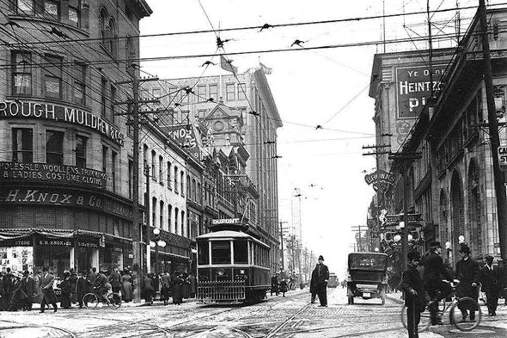 Cyclists occupy the edge of the frame at a busy Queen & Yonge, 1910