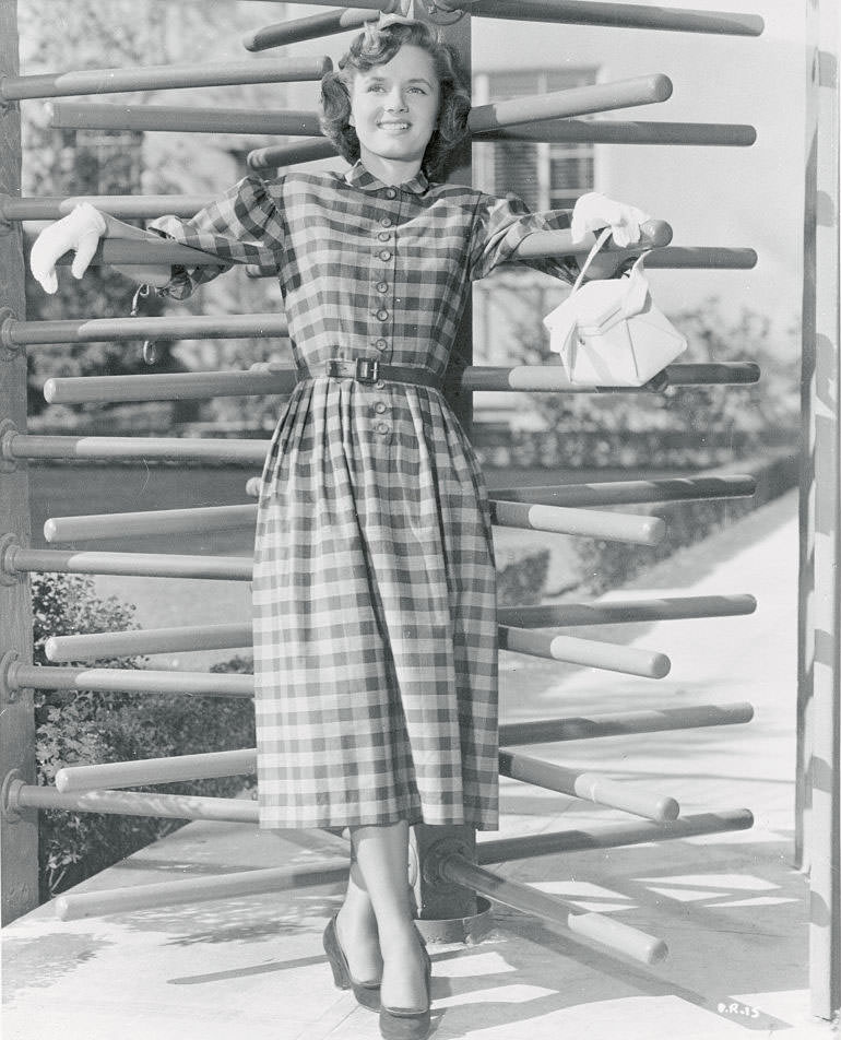 Debbie Reynolds wears a button-front plaid cotton dress with demure, rounded collar and three-quarter sleeves, 1950.