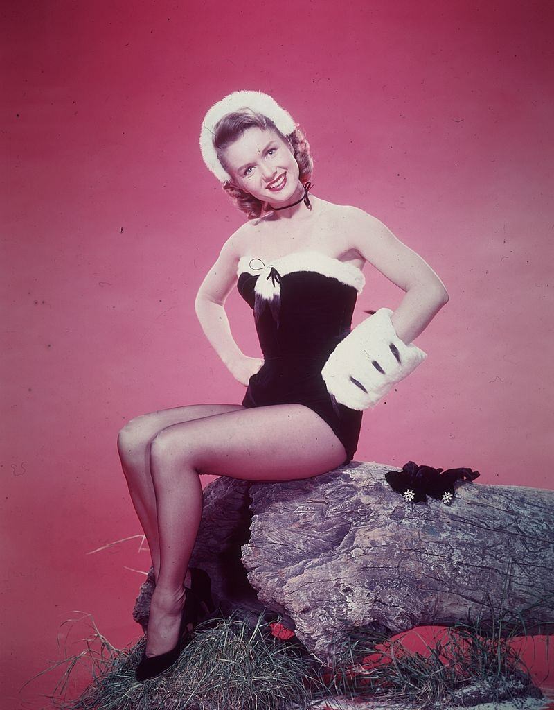 Debbie Reynolds sitting on the base of an overturned tree, 1955.