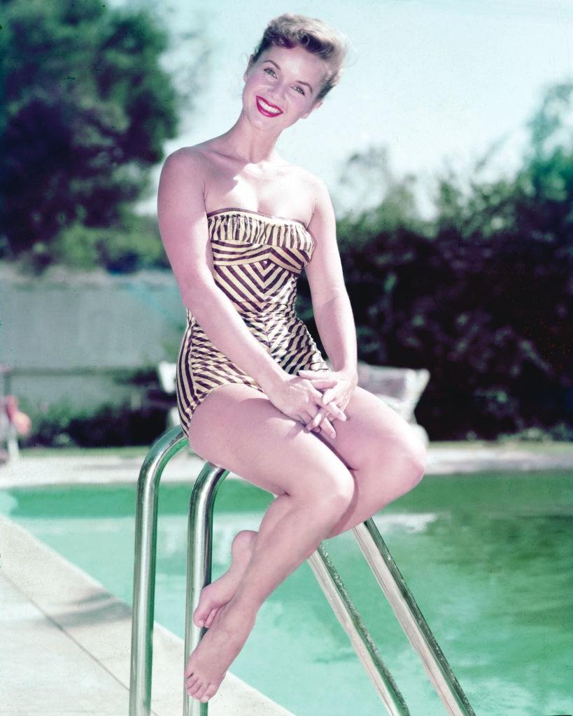 Debbie Reynolds wearing a swimsuit, sitting beside a swimming pool, 1955.