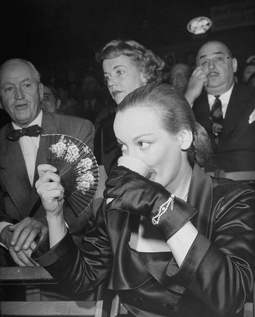 Faye Emerson drinking while fanning herself down during a Roller Skating Derby, 1950.