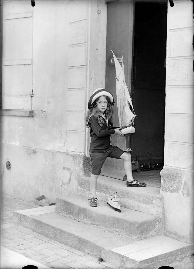 Girl on the steps of the family house with his toy boats, circa 1900