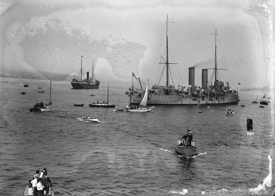 Spectators swarm around the H.C.M.S. Rainbow with the Komagata Maru in the background.