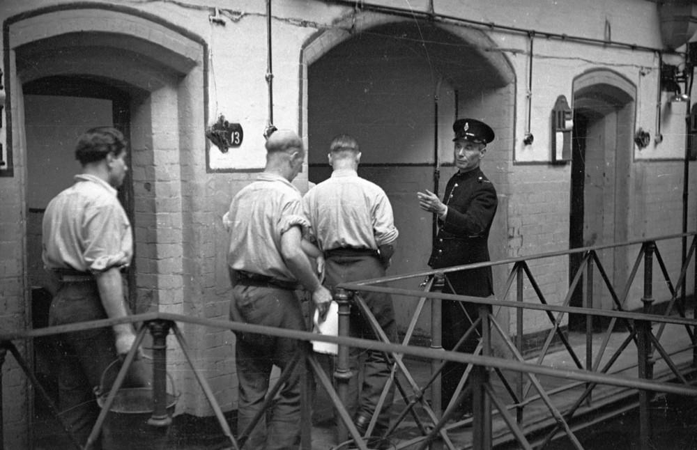 A prison officer supervising prisoners as they take out their night-slops at Strangeways Prison.