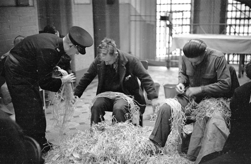 A prison officer supervising prisoners who are untying knots in Post Office string at Strangeways Prison.