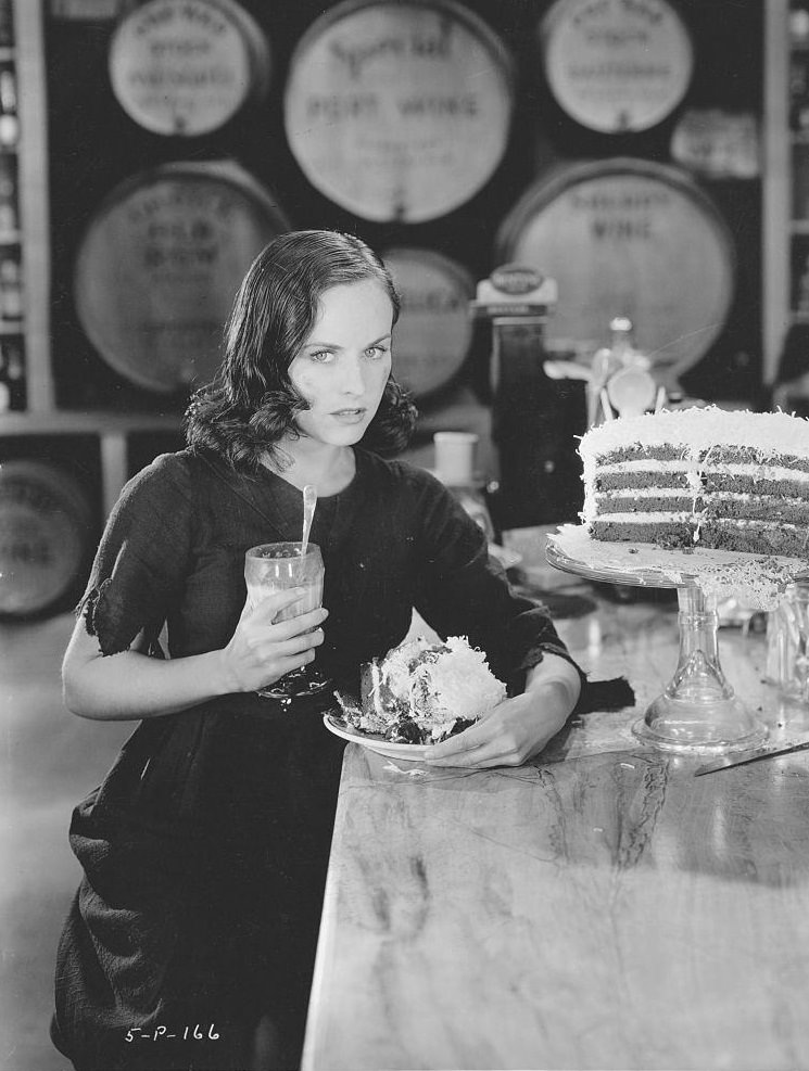 Paulette Goddard holds a plate of cake and a milkshake, 1936.