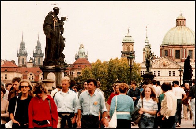 Students and shoppers cross the Charles Bridge at lunchtime. St Nicholas church is in the background