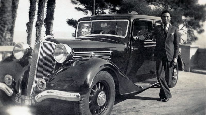 A fellow in a single-breasted suit posing with a Renault Vivastella on a sunny summer's day. The car is registered in the city of Paris, 1938