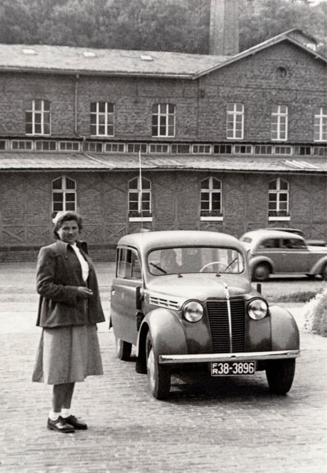 A young lady posing with a Renault Juvaquatre Break in front of a brick-built factory, circa 1952