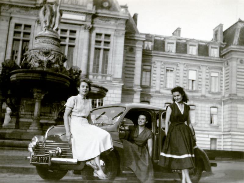 Three fashionable ladies posing with a Renault 4 CV in front of a historic palace.