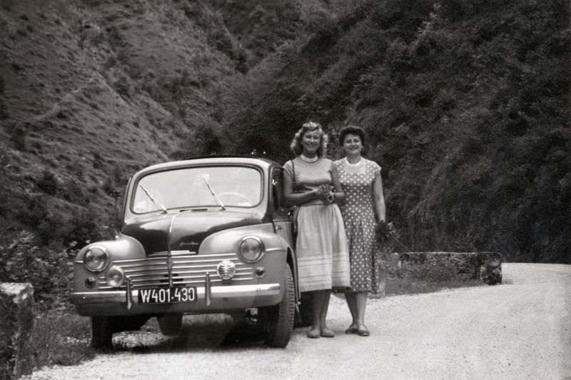 Two fashionable ladies posing with a two-tone Renault 4 CV on a gravelled mountain road.