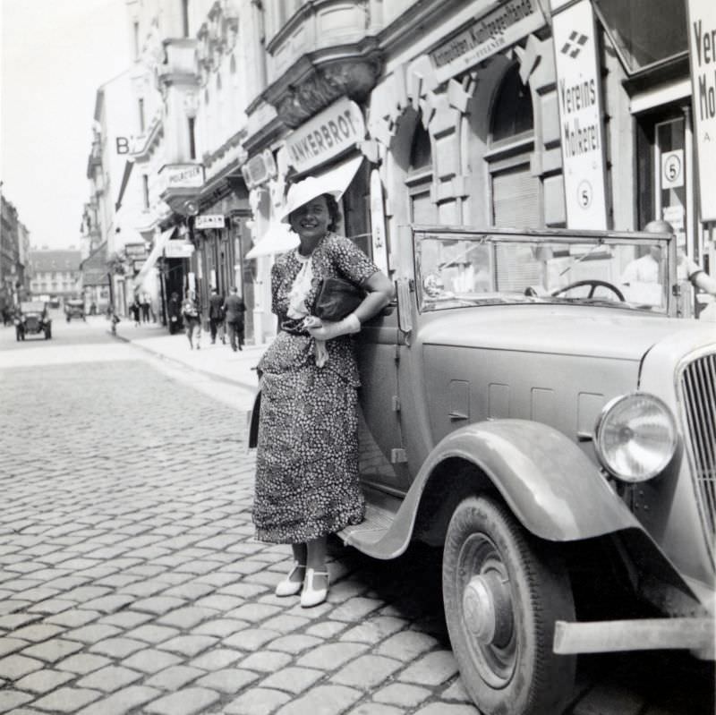 A cheerful lady posing with a Renault Monaquatre Cabriolet-Spider convertible in a cobbled city street, 1935