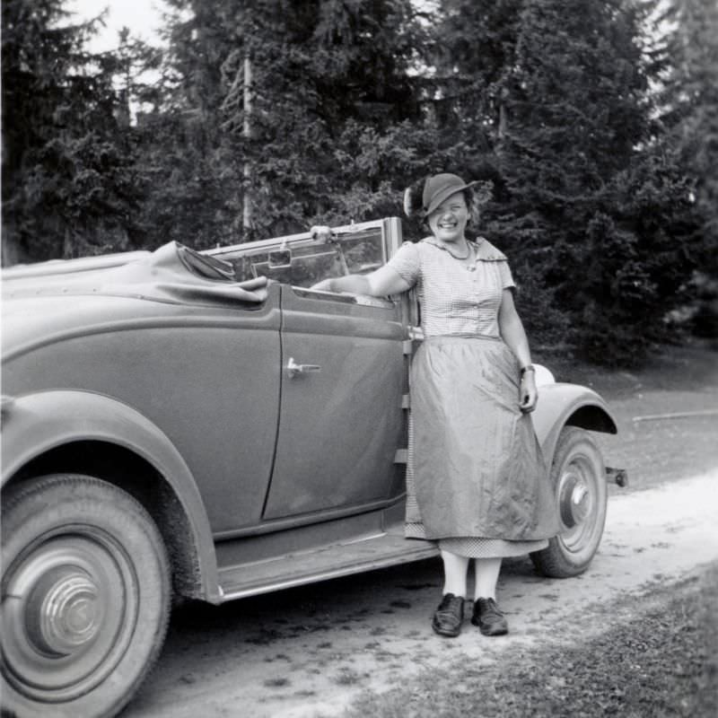 A cheerful lady posing with a Renault Monaquatre Cabriolet-Spider convertible on a dirt road in the countryside, 1935