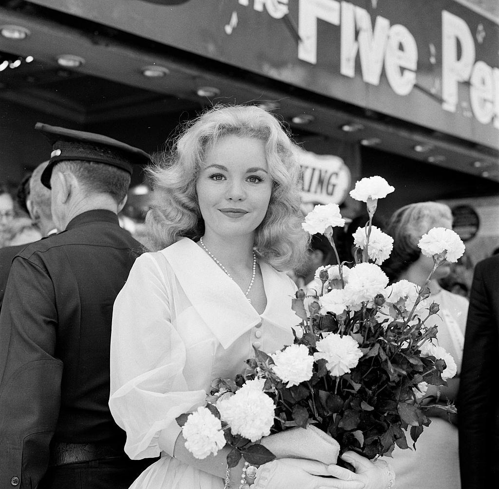 Actress Tuesday Weld poses with a bouquet of flowers during her movie premiere of "The Five Pennies", 1959.