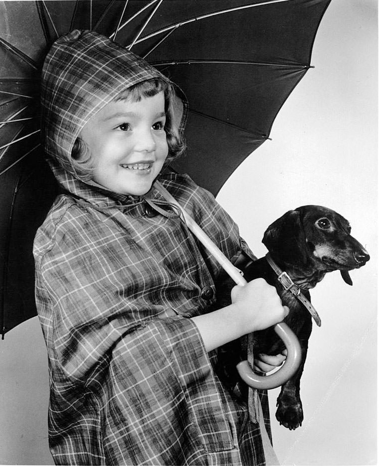 Tuesday Weld holding dog in rain gear in publicity portrait, 1948.