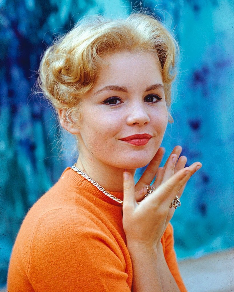 Tuesday Weld wearing an orange top and a gold chain around her neck, 1965.