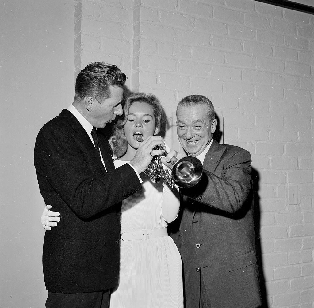 Tuesday Weld with Danny Kaye as she pretends to play a trumpet during an event in Los Angeles, 1958.