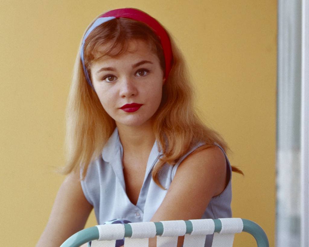 Tuesday Weld in a blue, sleeveless top and a red and blue headband, as she sits in a deckchair, 1950s.