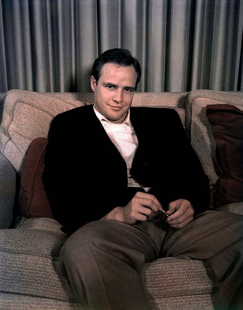 Marlon Brando sitting on a couch and smiling, 1950.