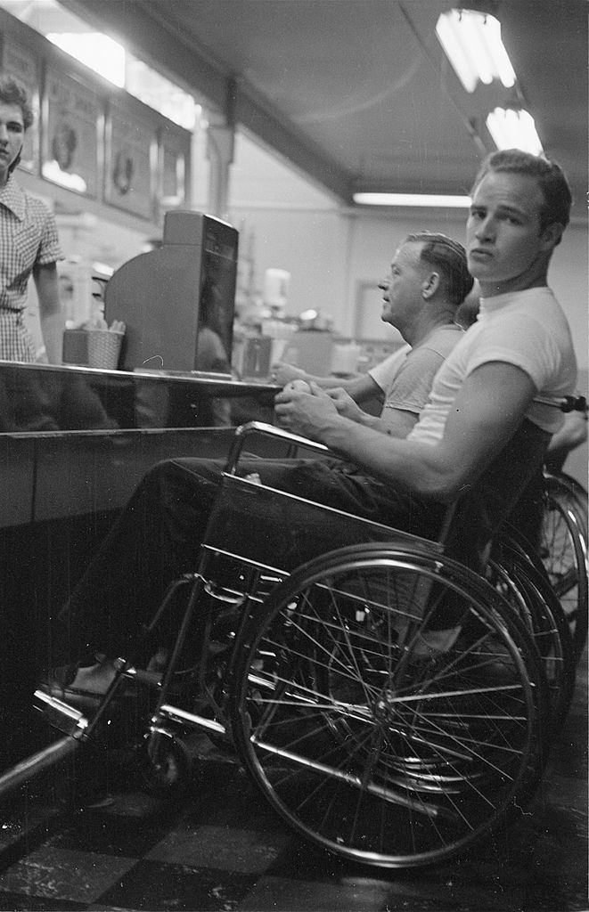 Marlon Brando sitting in a wheelchair at a coffee shop counter, during the filming of "The Men".