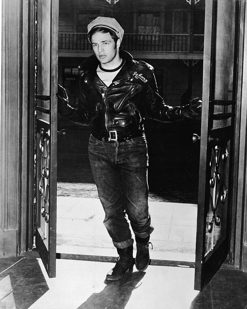 Marlon Brando stands in an open doorway, wearing a leather jacket and hat, 1953.