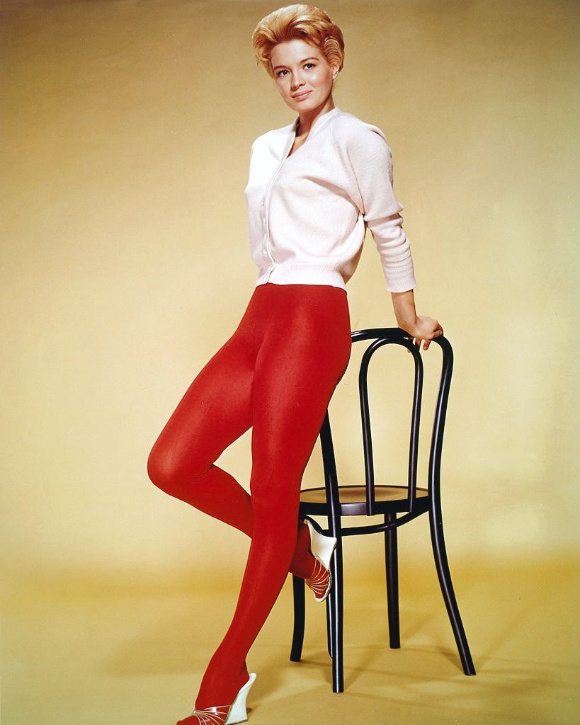 Angie Dickinson wearing a white cardigan and red tights, 1955.