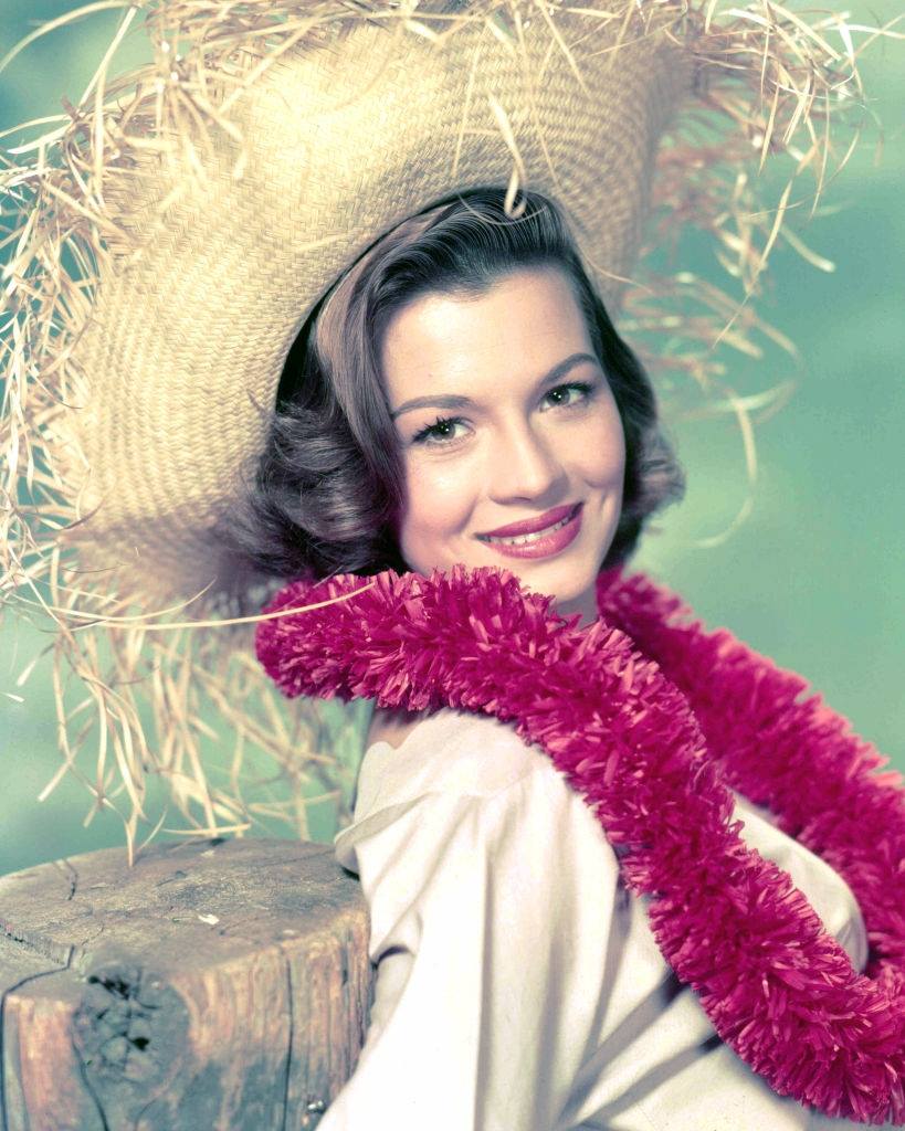 Angie Dickinson wearing a pink garland and a straw hat, 1955.