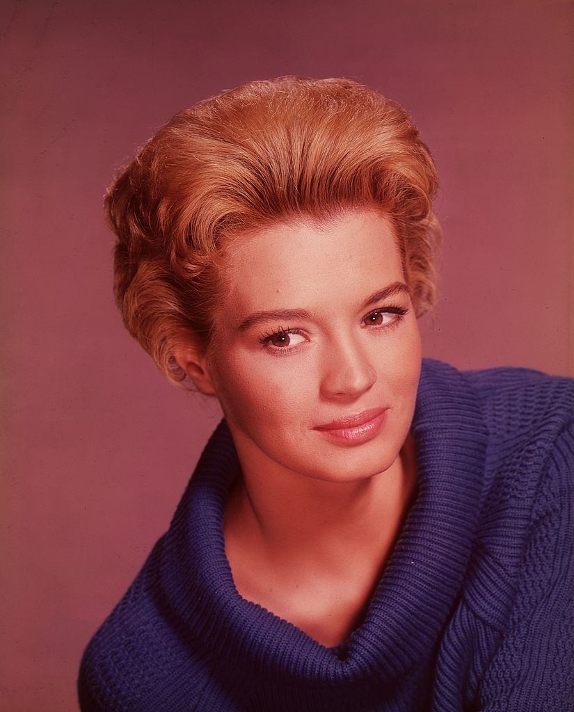 Angie Dickinson smiling in a blue cowl-necked sweater, 1960.