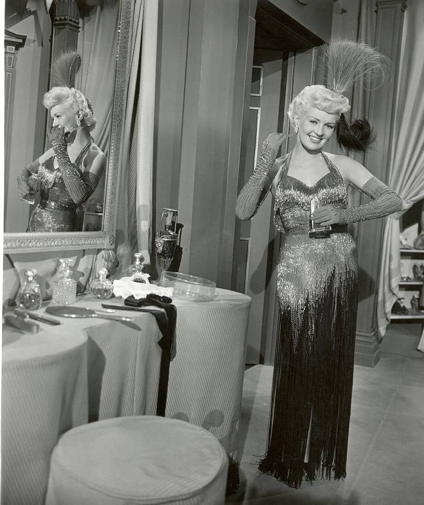 Betty Grable in a scene from the movie, "My Blue heaven," posing in an elaborate gown and holding a perfume bottle, 1950s.