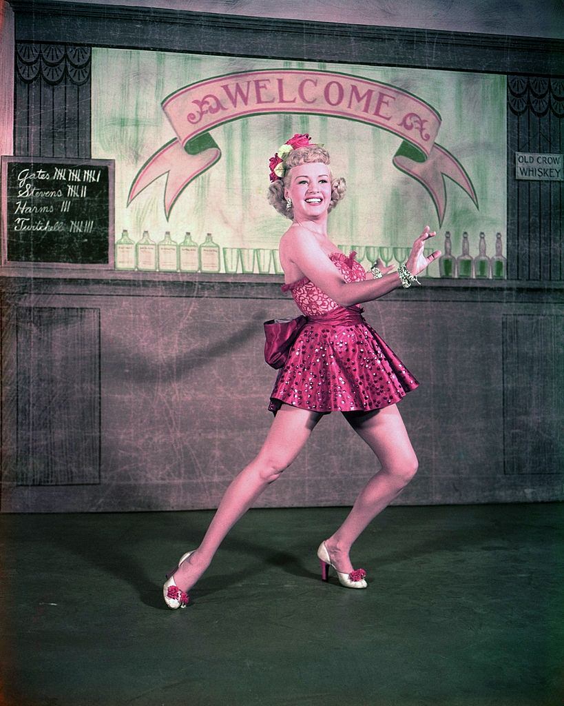 Betty Grable wearing a short red dress as she holds a dance pose, 1940.