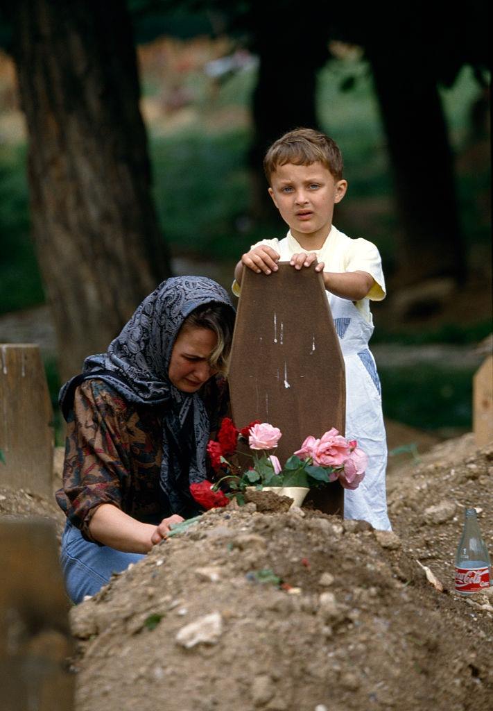 A young Bosnian boy and his mother mourning their father and husband, respectively, at his grave.