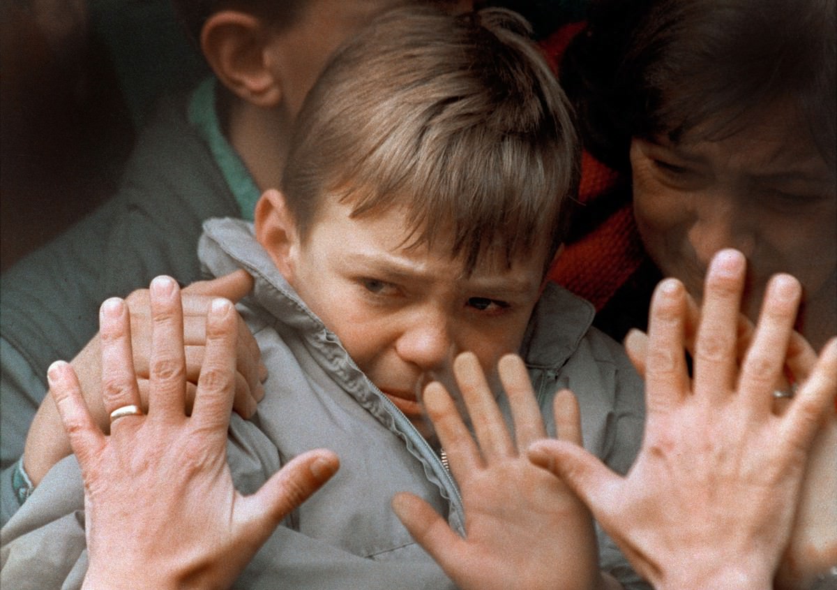 A father's hands press against the window of a bus carrying his tearful son and wife to safety from the besieged city of Sarajevo during the Bosnian War on November 10, 1992