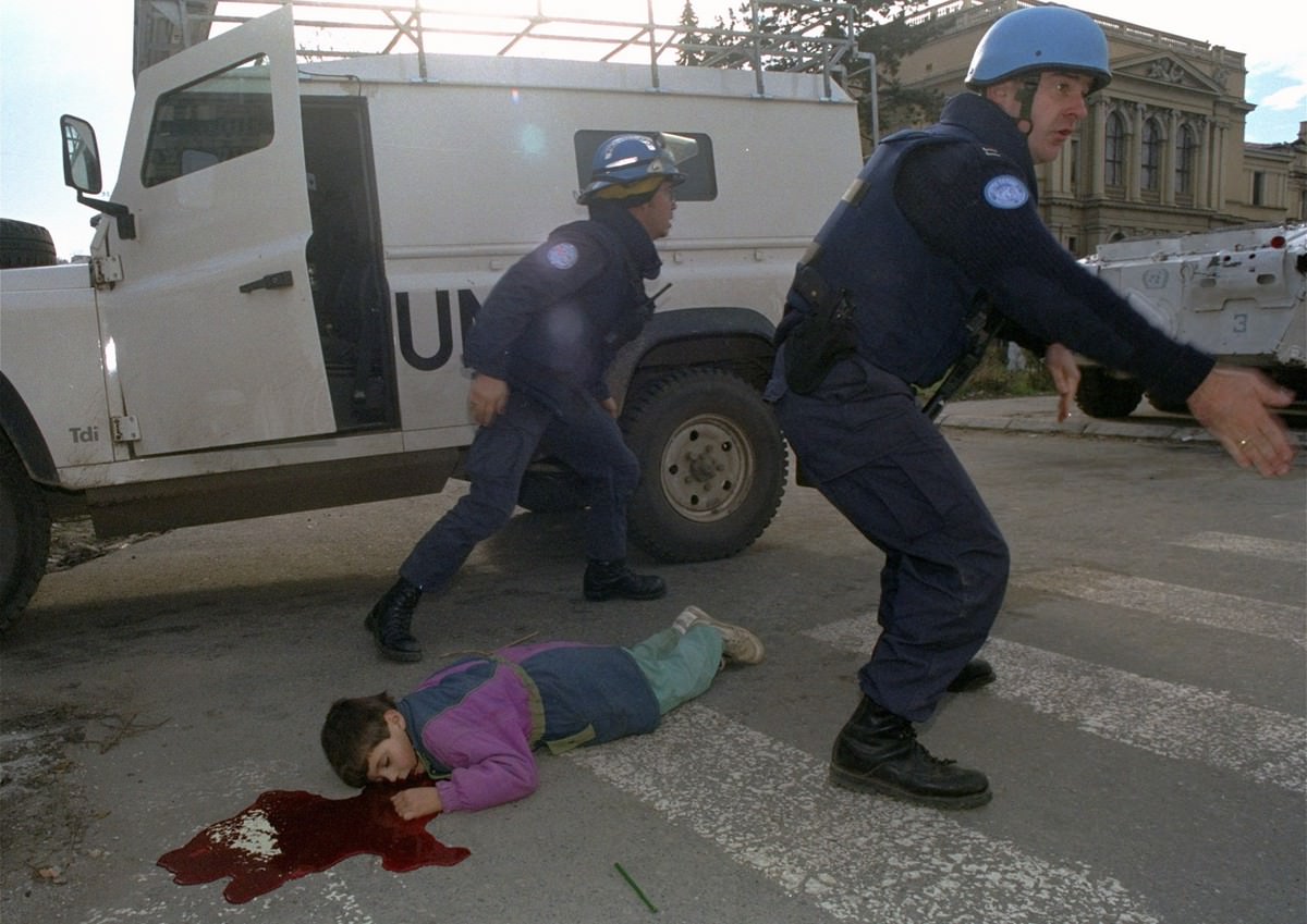 Seven-year-old Nermin Divovic lies mortally wounded in a pool of blood as unidentified American and British U.N. firefighters arrive to assist after he was shot in the head in Sarajevo Friday, November 18, 1994.