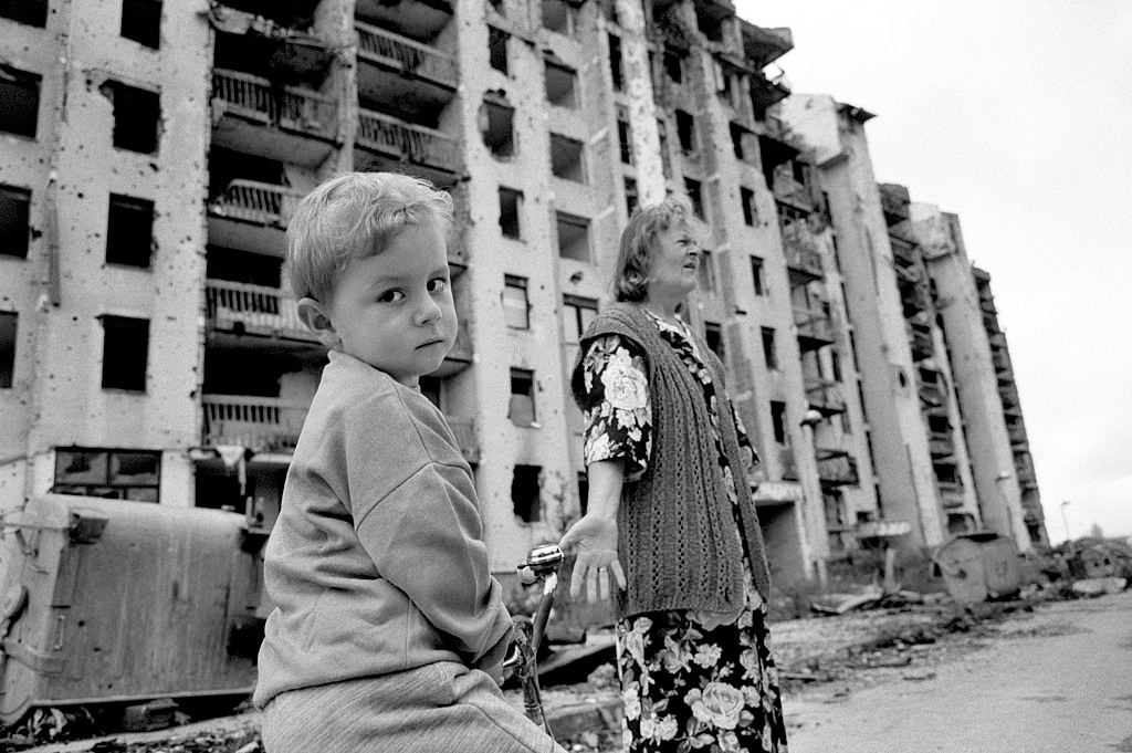 A traumatised child and his grandmother outside their devastated shell damaged apartment block.