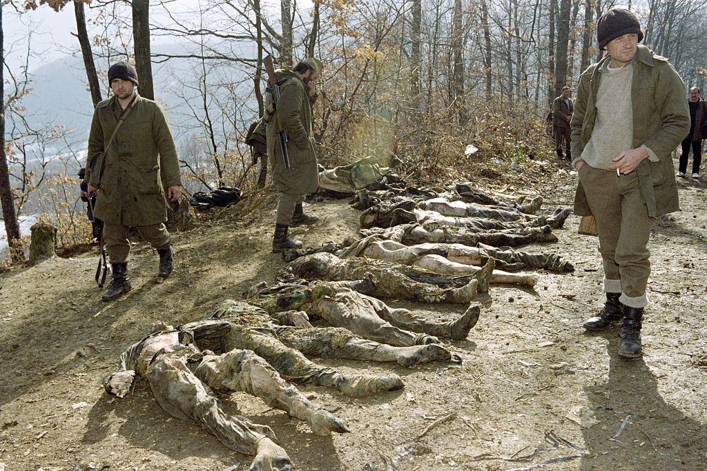 Bosnian Serbs stand near the bodies of the 24 mutilated men discovered in a mass grave, they say were killed by Bosnian Moslems in Eastern Bosnian village of Kamenica on February 17, 1993.