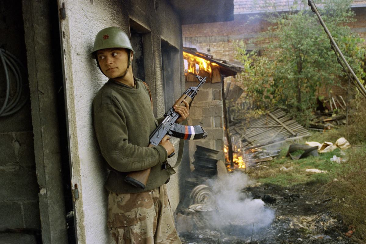 A Serbian soldier takes cover by a burning house in the village of Gorica, Bosnia-Herzegovina, on October 12, 1992.